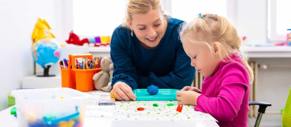 Toddler girl in child occupational therapy session doing sensory playful exercises with her therapist.