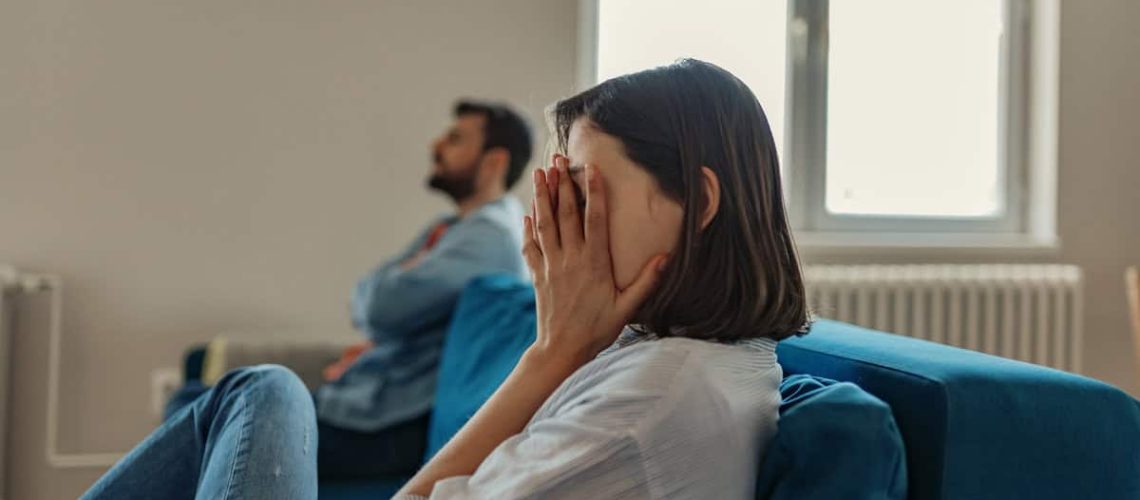 Unhappy Couple After an Argument in the Living Room at Home. Sad Pensive Young Girl Thinking of Relationships Problems Sitting on Sofa With Offended Boyfriend, Conflicts in Marriage, Upset Couple After Fight Dispute, Making Decision of Breaking Up Get Divorced