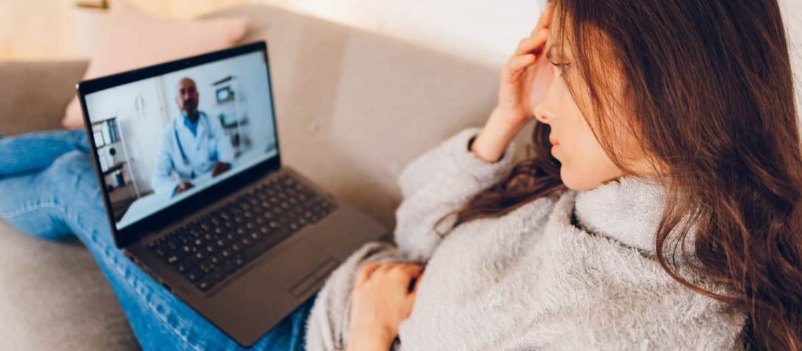 Young beautiful woman having video call with doctor using laptop at home