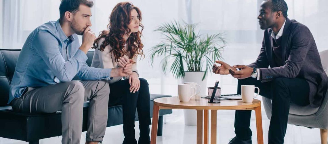 Smiling african american psychiatrist talking to young couple in office about infertility