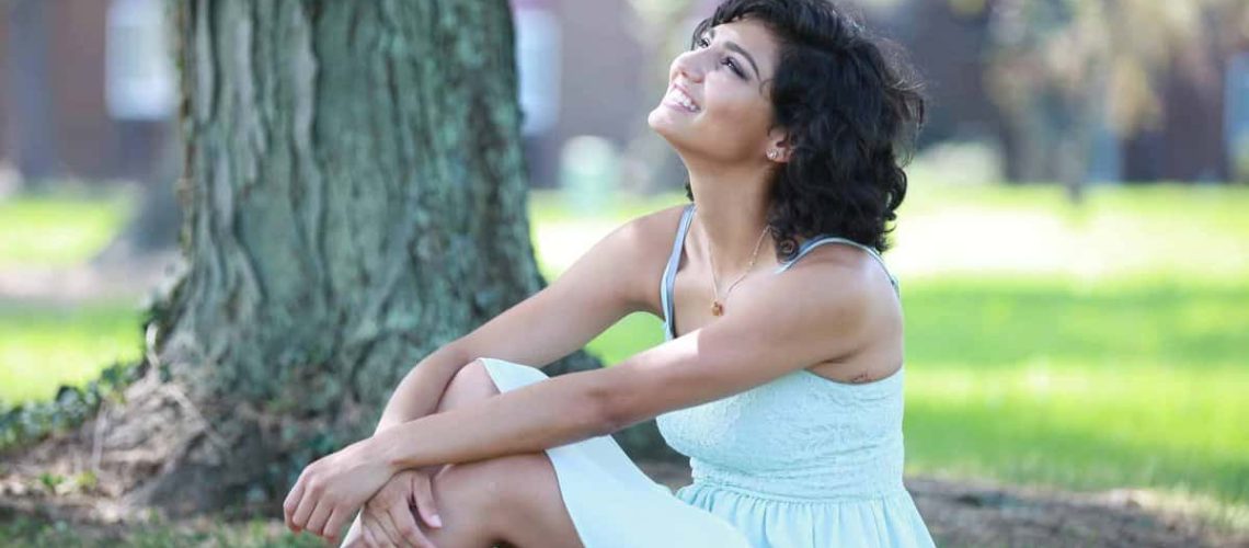 Beautiful hispanic girl sitting on the grass looking to the sky