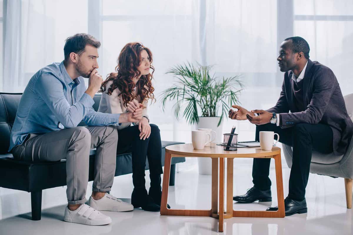 Smiling african american psychiatrist talking to young couple in office about infertility